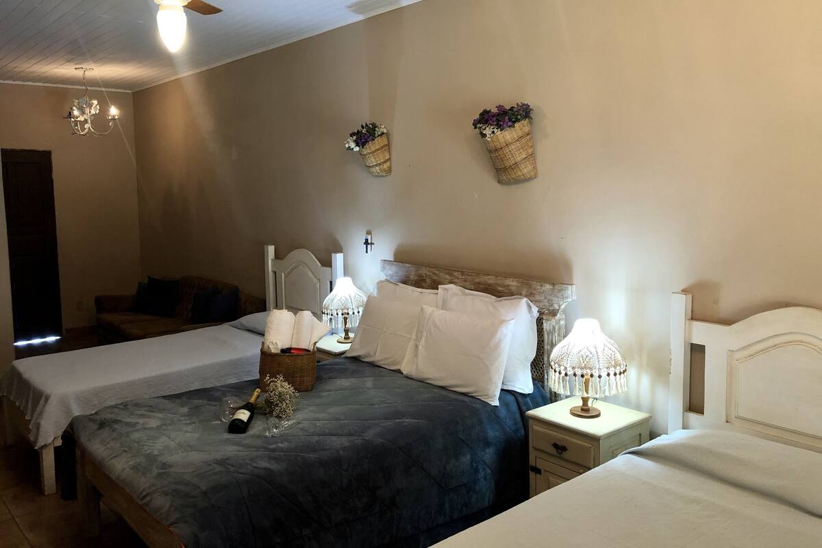 A bedroom with a large bed, two bedside tables, a ceiling fan, a chandelier, and wall-mounted baskets with flowers.
