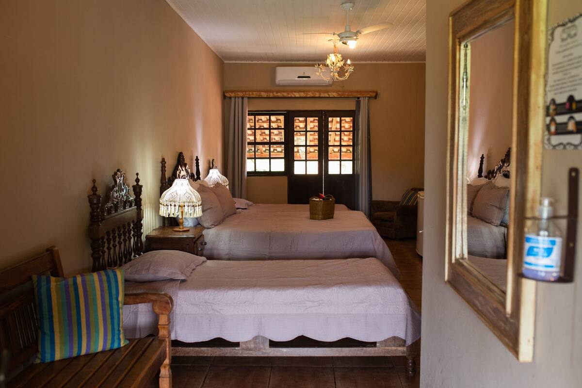 A bedroom with two beds, a wooden bench, a lamp, and a mirror.