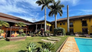A courtyard with a swimming pool, palm trees, and a yellow building with a tiled roof. - Maria Barbosa Tiradentes Hotel and Spa (Tiradentes)