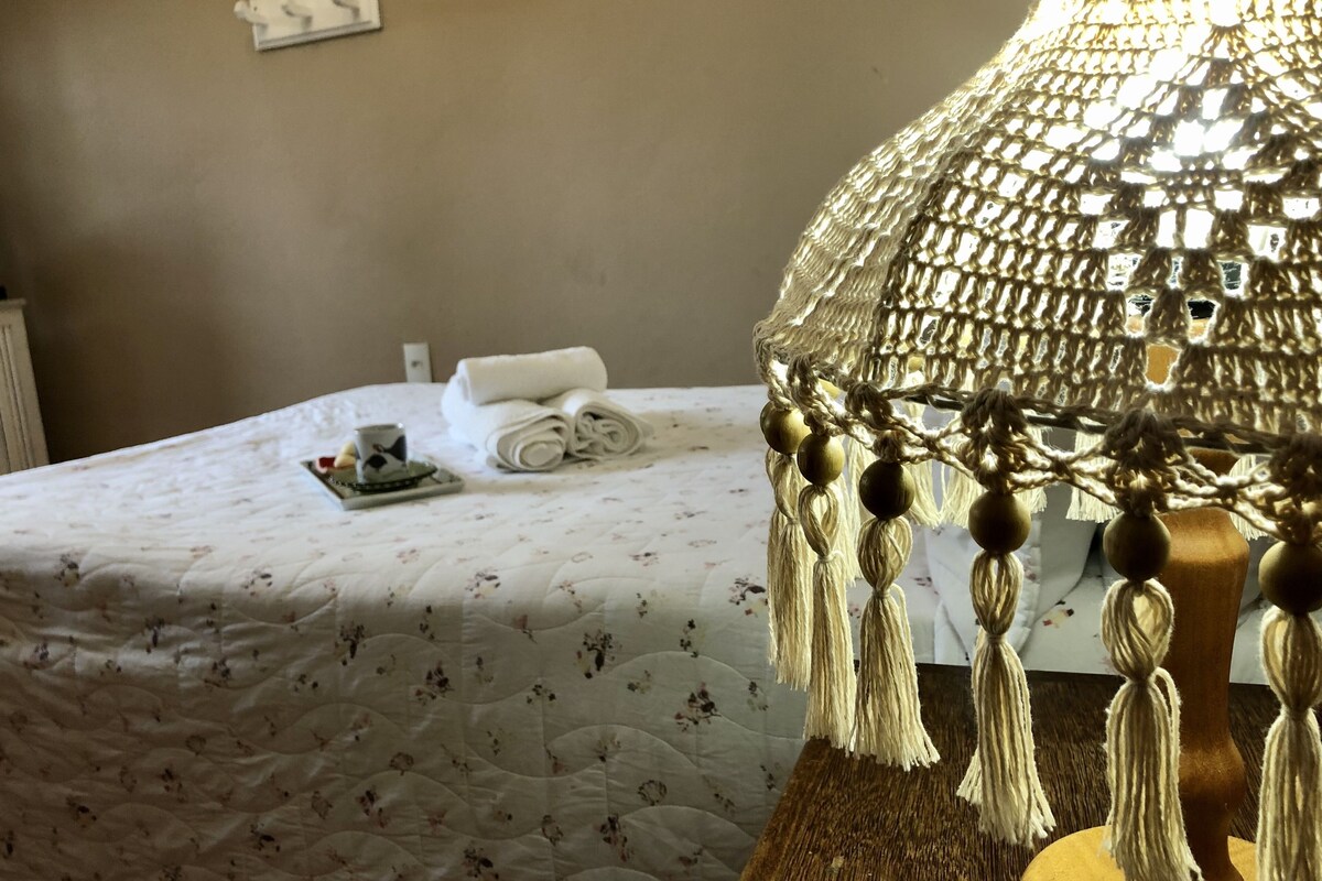 A bed with a floral quilt, a rolled towel, and a tray with a cup and a small item.