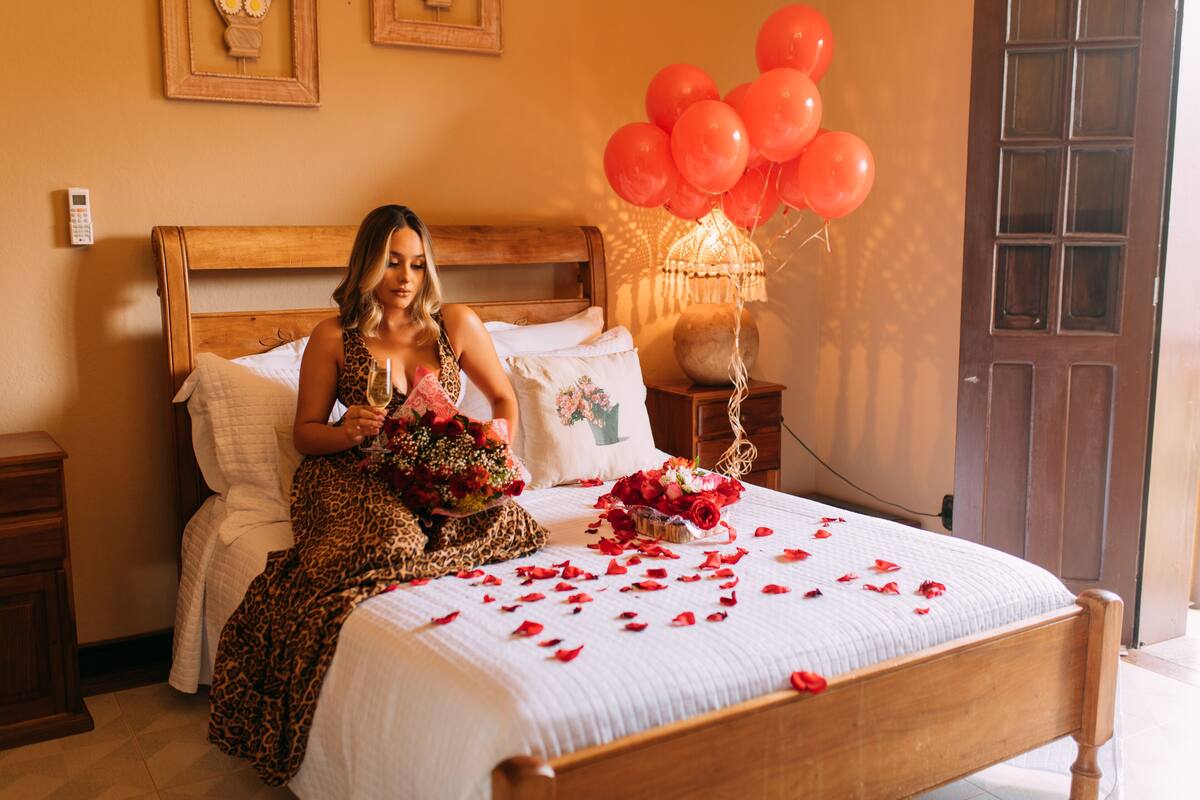 A bed with rose petals, a bouquet of flowers, and red balloons.