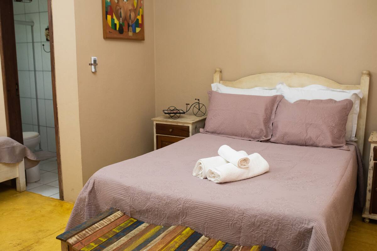 A neatly made bed with a pink bedspread and pillows, a wooden headboard, and a small bedside table with a bicycle decoration.
