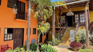 A two-story building with a yellow facade, a staircase leading to the upper floor, and a variety of potted plants and hanging decorations. - Maria Barbosa Tiradentes Hotel and Spa (Tiradentes)