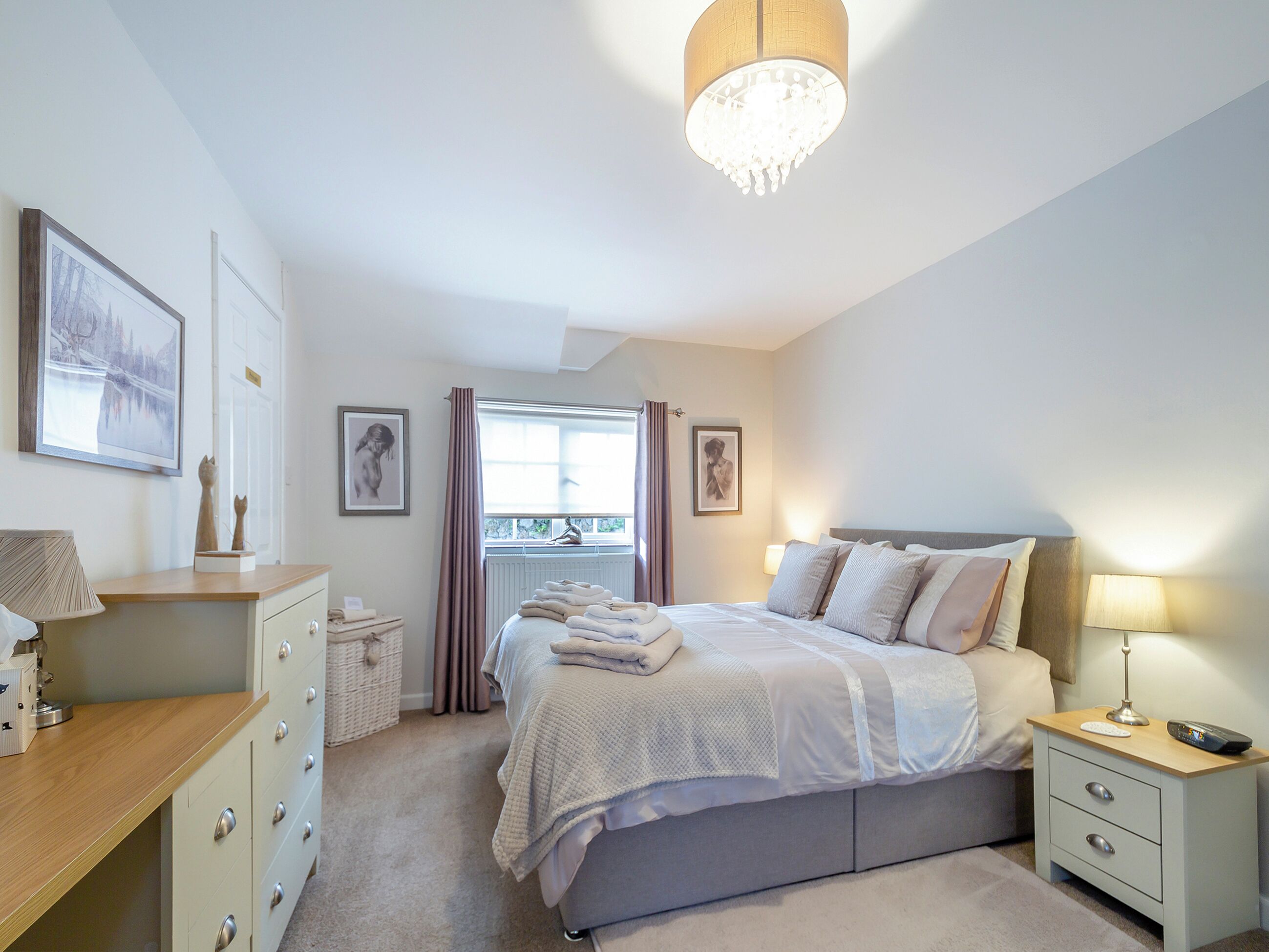 Une chambre à coucher avec un lit, des tables de chevet, un bureau et une fenêtre avec des rideaux.
