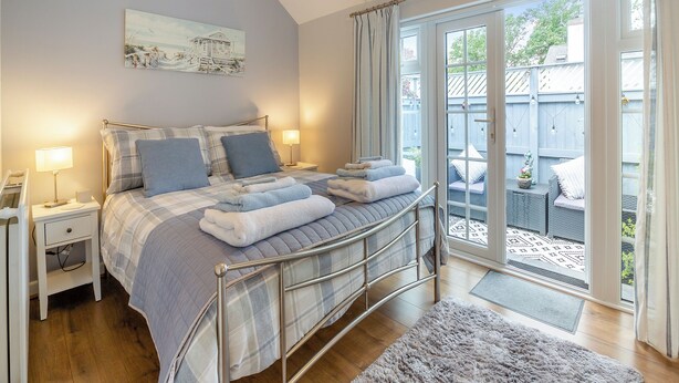 Ein Schlafzimmer mit einem Bett, Nachttischen, einer Chandelüster, einem Gemälde und Blick ins Freie.