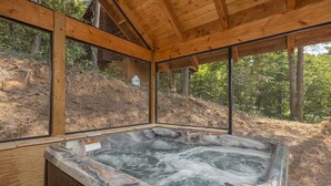 Un bain à remous doté d’une terrasse en bois et de grandes fenêtres donnant sur une colline boisée.