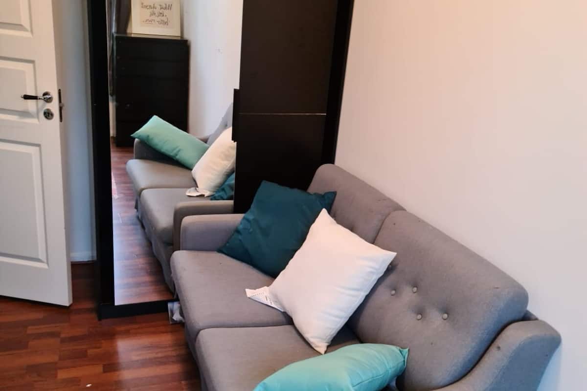 A room with a grey sofa, teal cushions, a wooden floor, and a door leading to another room.