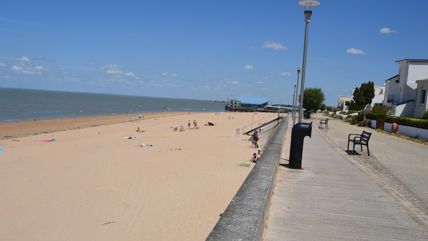 A beach with a wooden walkway, beach chairs, and umbrellas.