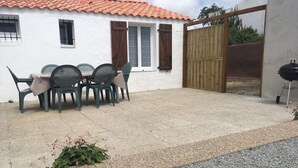 A patio with outdoor seating, a barbecue grill, and a white building with a tiled roof.