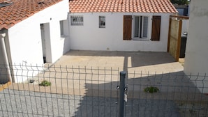 A fenced courtyard with a tiled roof, a small building with a window and shutter, and a gate.