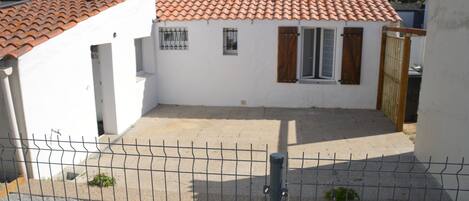 A fenced courtyard with a tiled roof, a small building with a window and shutter, and a gate.