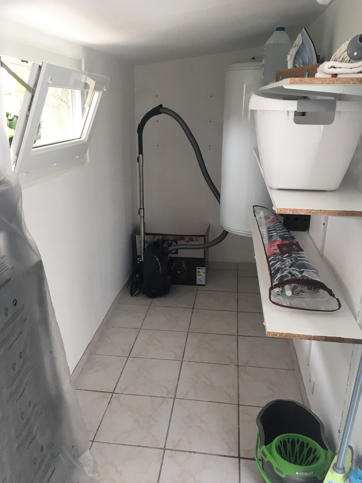 A laundry room with a vacuum cleaner, a washing machine, and shelves with folded clothes.