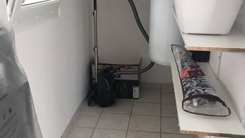 A laundry room with a vacuum cleaner, a washing machine, and shelves with folded clothes.