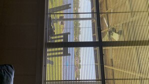 A window with vertical blinds, a view of a building outside, and a ceiling fan inside.