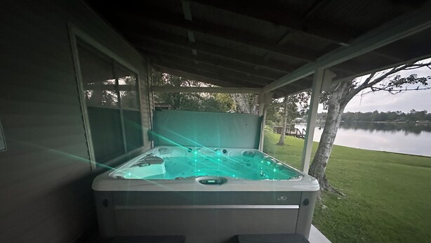 A hot tub with a glass enclosure, two footrests, and a view of a lake.