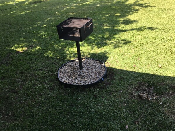 Un barbecue portable doté d’une base ronde et d’un dessus carré, placé sur une pelouse.