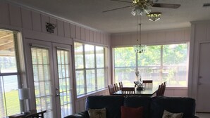 A living room with a sectional sofa, two ottomans, a dining table with chairs, and a ceiling fan.