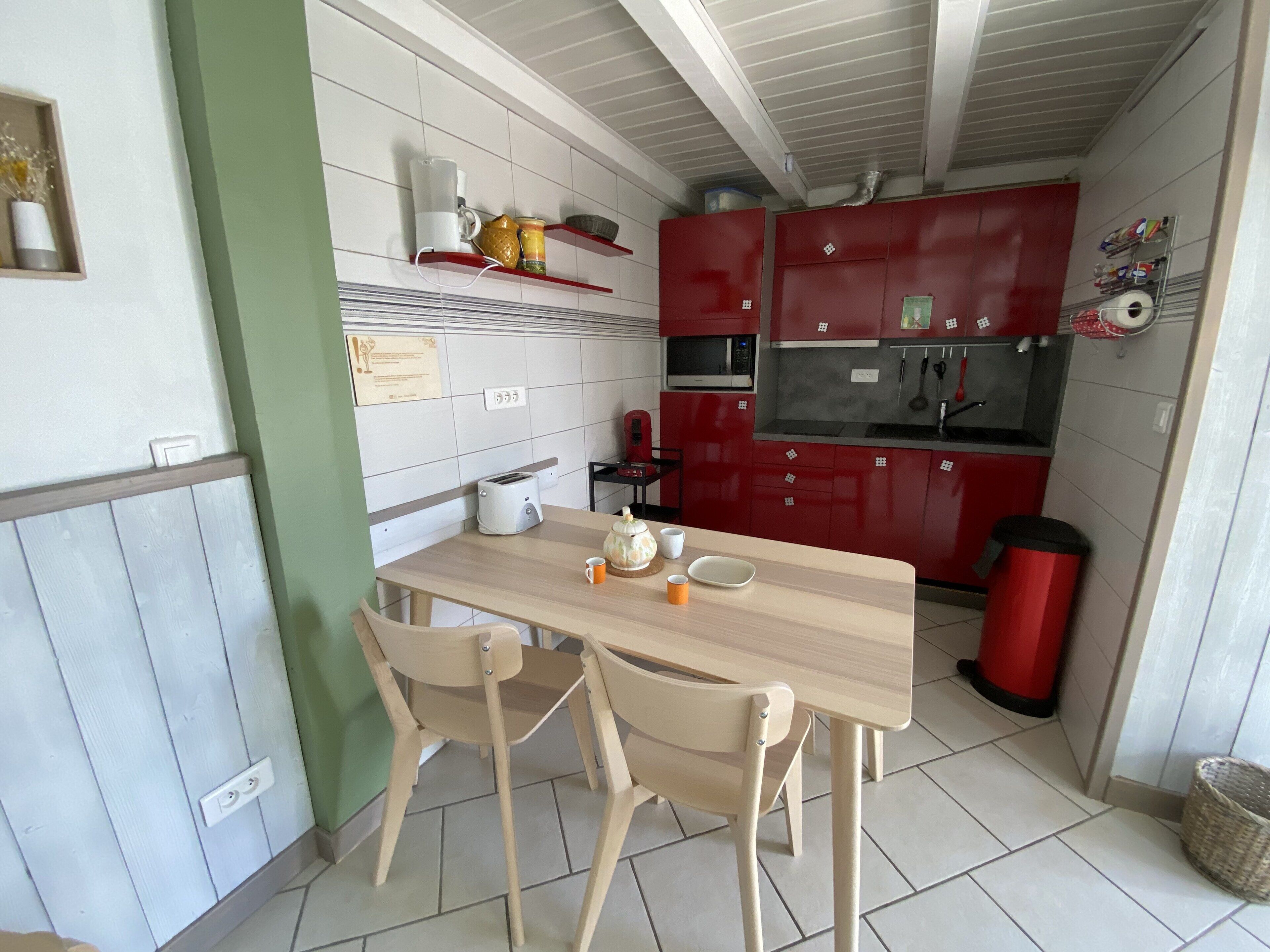 Una cocina compacta con una mesa de madera, dos sillas, un microondas rojo y un lavamanos.