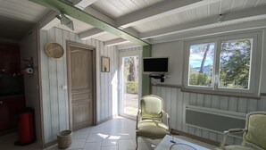 A room with a wooden door, a television mounted on the wall, and a window with a view of trees and hills.