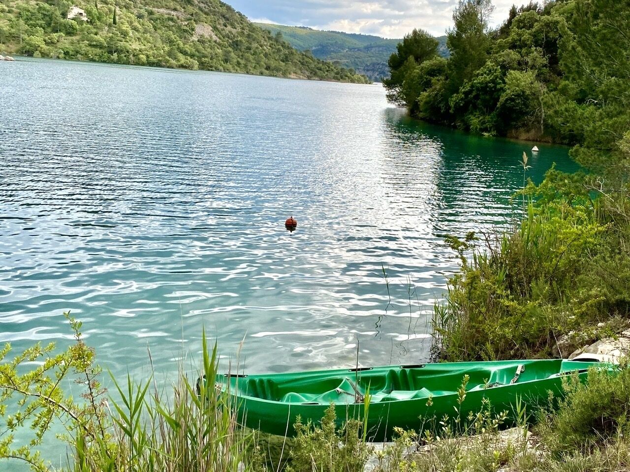 A calm lake with a green boat docked on the shore.