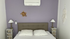 A bedroom with a bed, two bedside tables with lamps, an air conditioner, and a wall decoration.