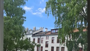 A multi-story building with a white facade and red window frames, surrounded by lush greenery and trees. - S12-3rd Floor Casa Grunerlokka (Oslo)