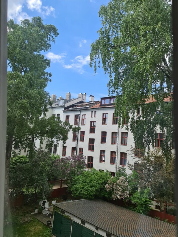 Un immeuble à plusieurs étages, doté d’une façade blanche et de cadres de fenêtres rouges, entouré d’une végétation luxuriante et d’arbres.