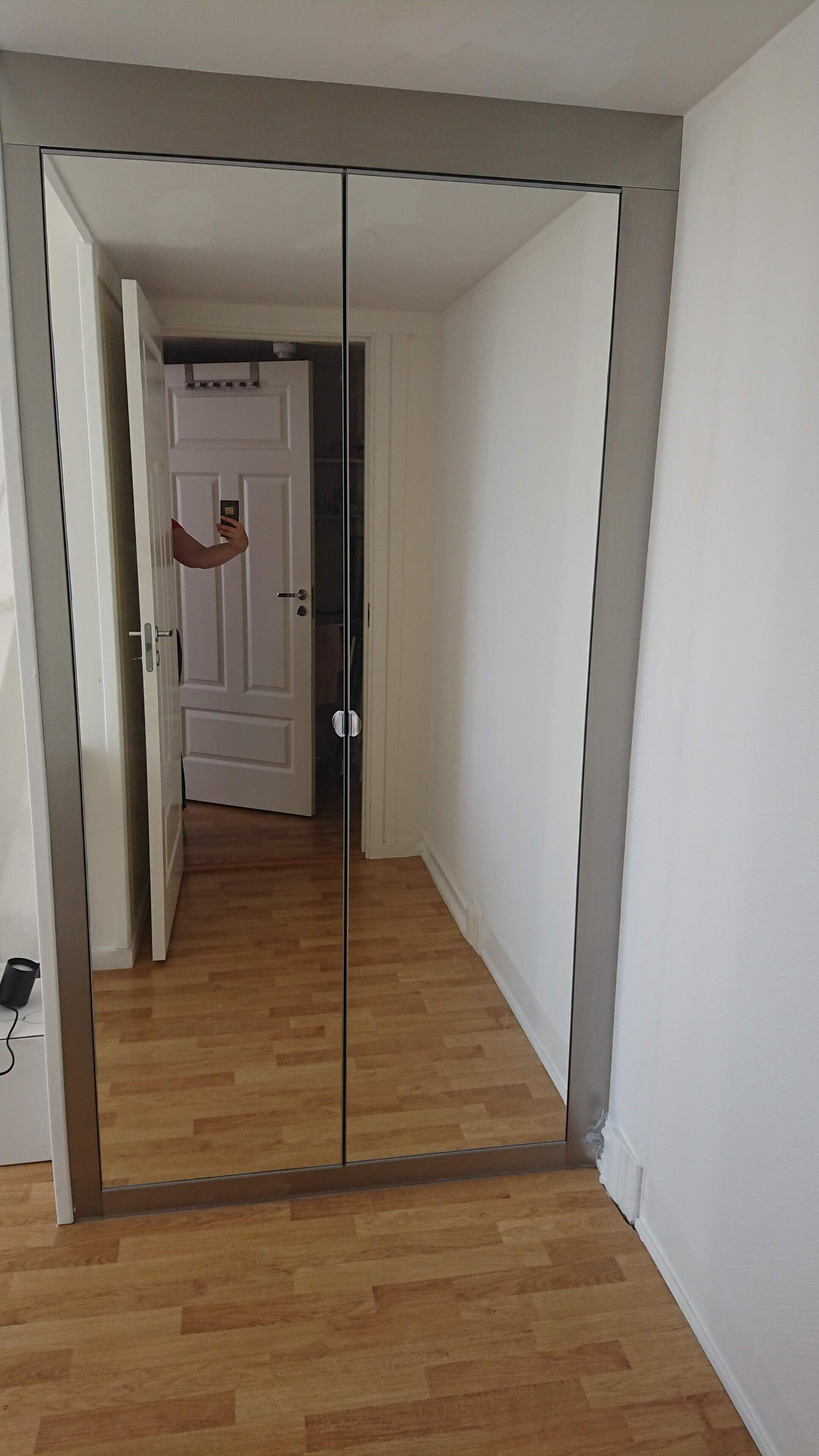 A room with a mirrored wardrobe, wooden flooring, and a white door.