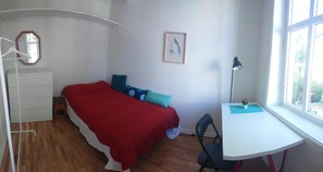 Une chambre à coucher comprenant un lit, un bureau, une chaise, une lampe suspendue, un miroir et une fenêtre.