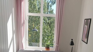 A cozy living room with a grey sofa, a small wooden table, a black chair, a floor lamp, and a window with curtains. - S12-3rd Floor Casa Grunerlokka (Oslo)