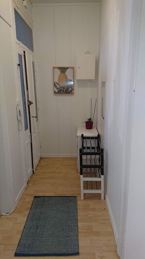 Un couloir étroit avec un plancher en bois, un banc noir et blanc, une plante en pot rouge et un tableau encadré accroché au mur.