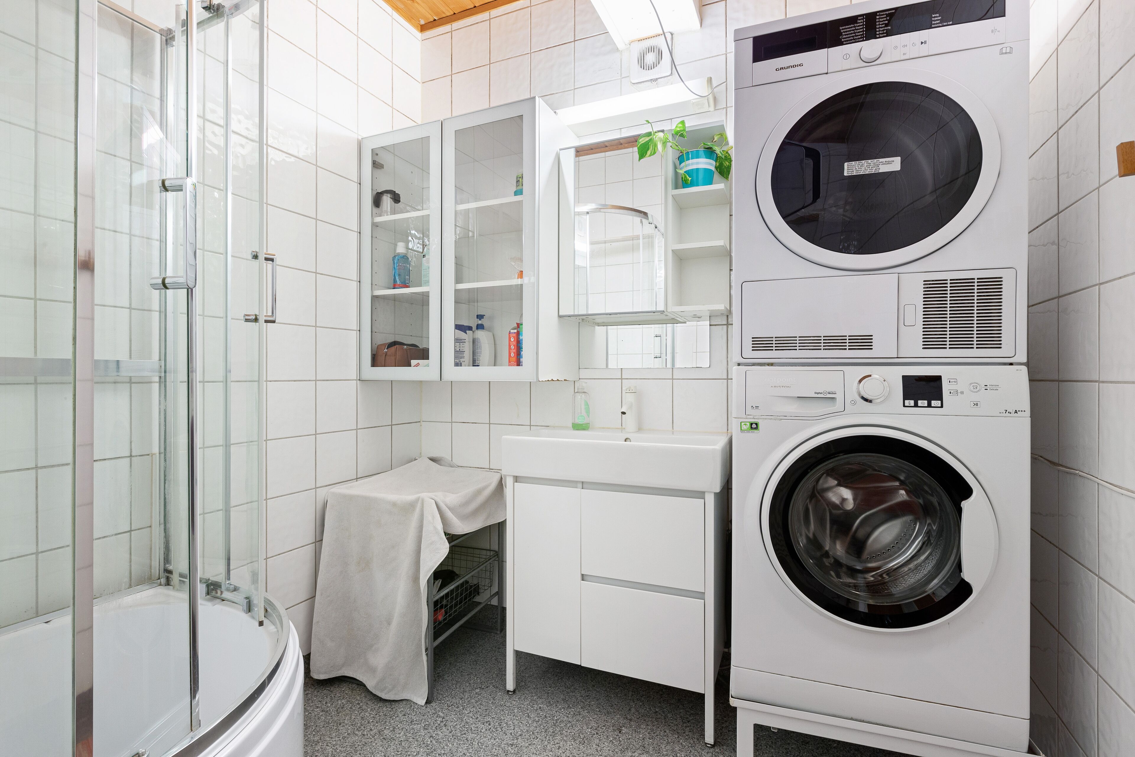 A modern bathroom with a glass-enclosed shower, a built-in washing machine, and a small vanity with a sink.