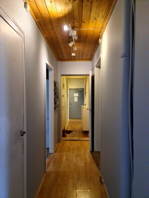A narrow hallway with wooden flooring and white walls, leading to a door at the end.