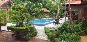 A pool surrounded by lush greenery, stone pathways, and wooden benches. - Tam Coc Melody Homestay (Nam Hoa Lu)