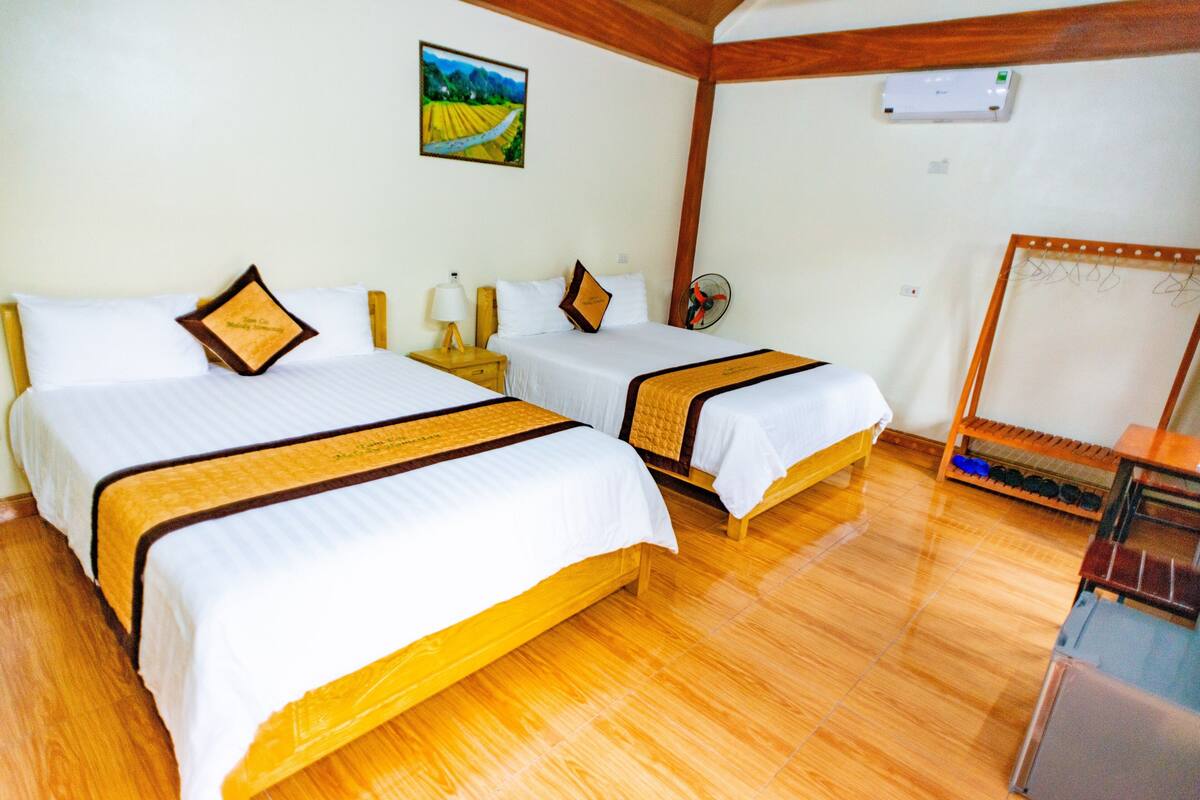 Une chambre d’hôtel avec deux lits, un plancher en bois, un ventilateur, une petite table et un tableau au mur.