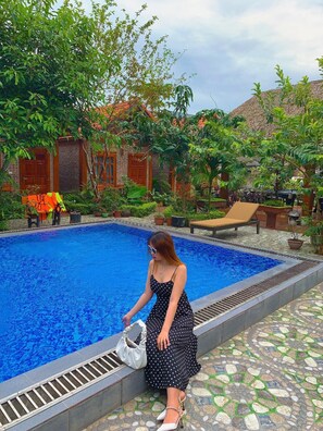 A swimming pool with a tiled edge, surrounded by greenery and a brick building. - Tam Coc Melody Homestay (Nam Hoa Lu)