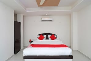 A bedroom with a bed, a nightstand, a wall-mounted air conditioner, and a door. - Hotel Balaka Inn (Bolpur)