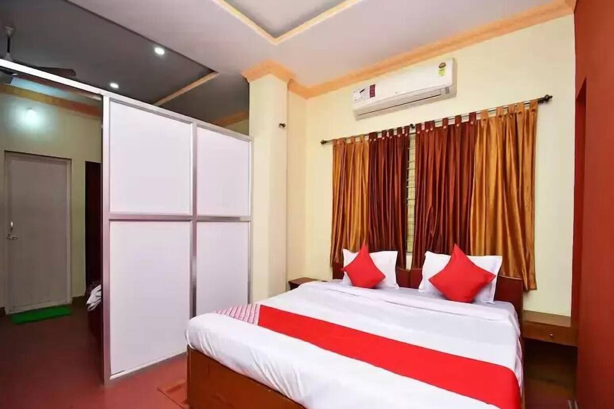 Quarto de hotel com cama, guarda-roupa, ar condicionado e janela com cortinas.