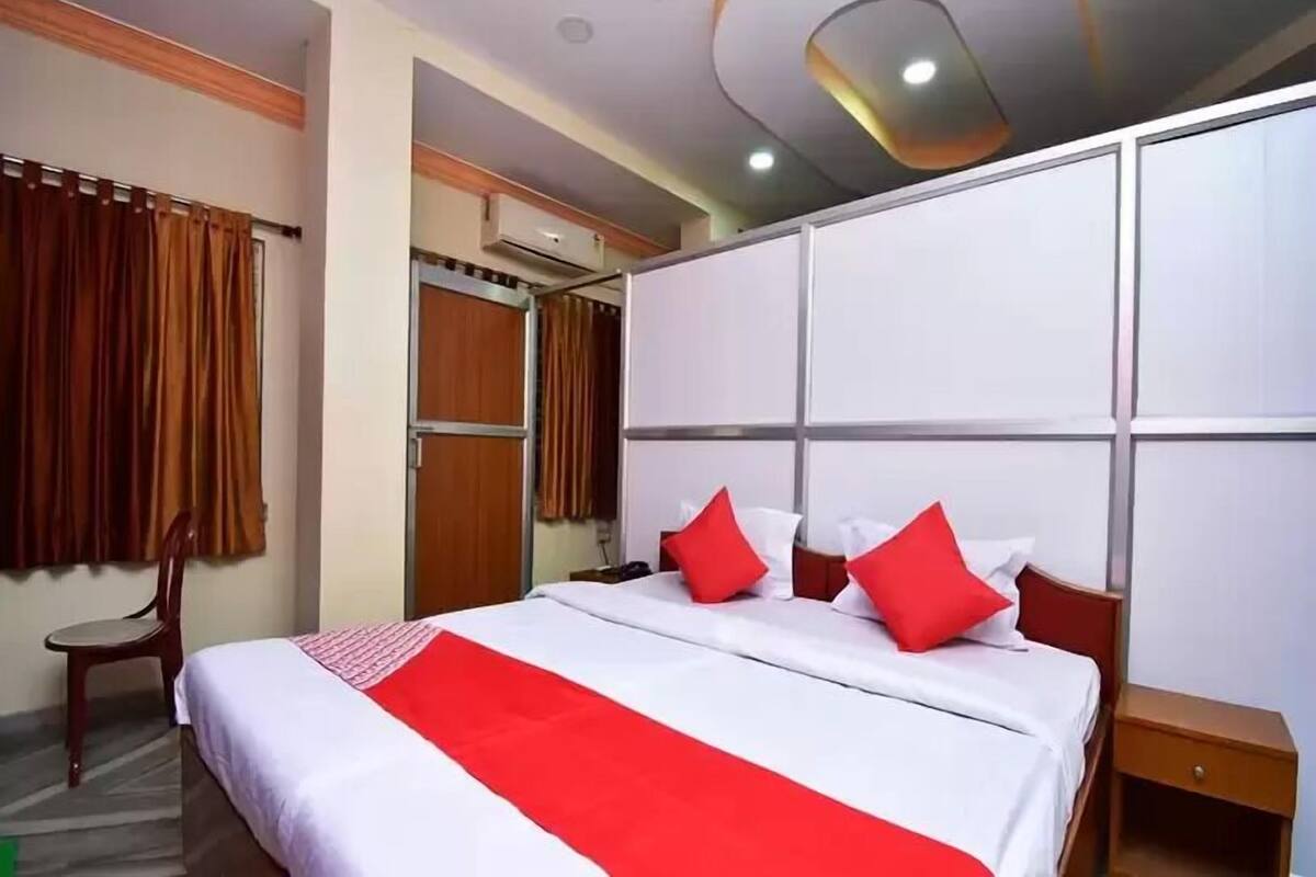 Quarto de hotel com uma cama grande, uma mesa de cabeceira de madeira, uma cadeira e um guarda-roupa.