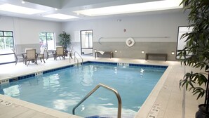 En indendørs swimmingpool med tydelige dybdemarkeringer, en redningsbøje og et opholdsområde med stole og et bord.