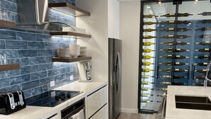 Una cocina moderna con un extractor de acero inoxidable, horno empotrado, refrigerador y una estantería para vinos con botellas.