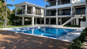 Una casa moderna de dos pisos con piscina, ventanas amplias y un área de patio techada.