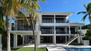 Una casa moderna de dos pisos con piscina, mobiliario exterior y palmeras.