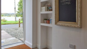 Una habitació amb una porta que dona a una vista d'un llac, una estant amb llibres i un cartell de pissarra que diu "Welcome to Printmaker's Cottage".