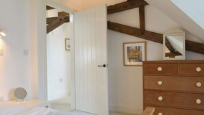Un dormitori amb un llit de fusta, un calaixera amb molts calaixos, una porta que dona a una altra habitació i un quadre al mur.