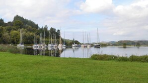 Un port esportiu amb diversos velers amarrats, envoltat de vegetació exuberant i turons al fons.