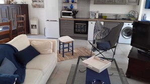 Un ambiente compatto con angolo cottura, divano, poltrona, televisore e lavatrice.