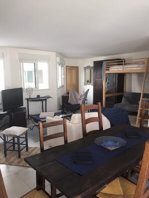 Un espace de vie compact comprenant un lit superposé, une table à manger, un téléviseur et un petit bureau.