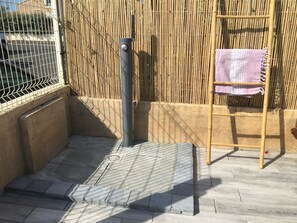 A tranquil outdoor space features a bamboo fence, a wooden ladder, and a metal pole with a round knob.