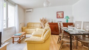A living room with a yellow sofa, a dining table set for four, and a wooden cabinet.